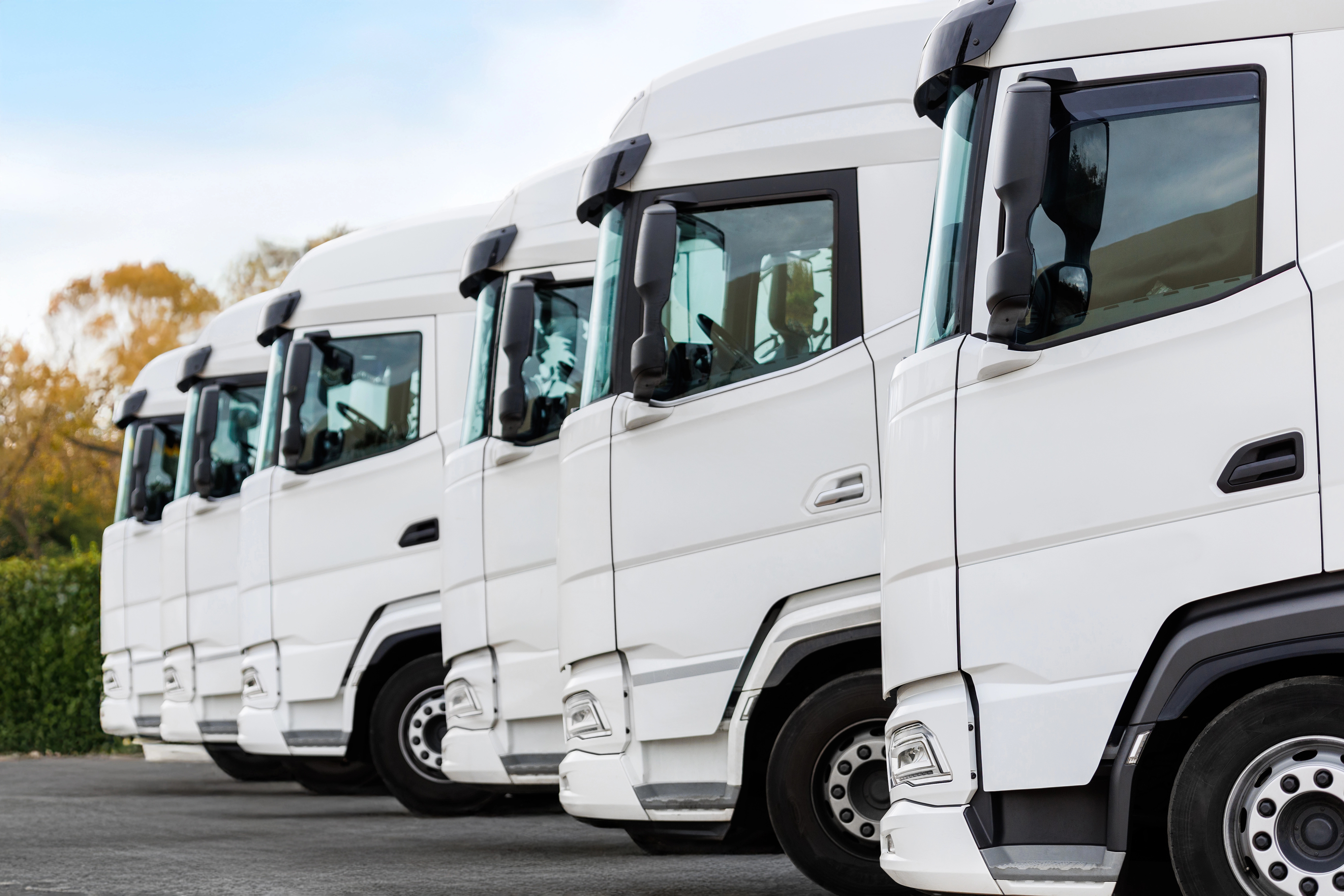 Fleet of new modern electric hybrid hydrogen or diesel white trucks parked in line row outdoors. Cargo freight industrial transportation logistics service. Commercial vehicles maintenance insurance.