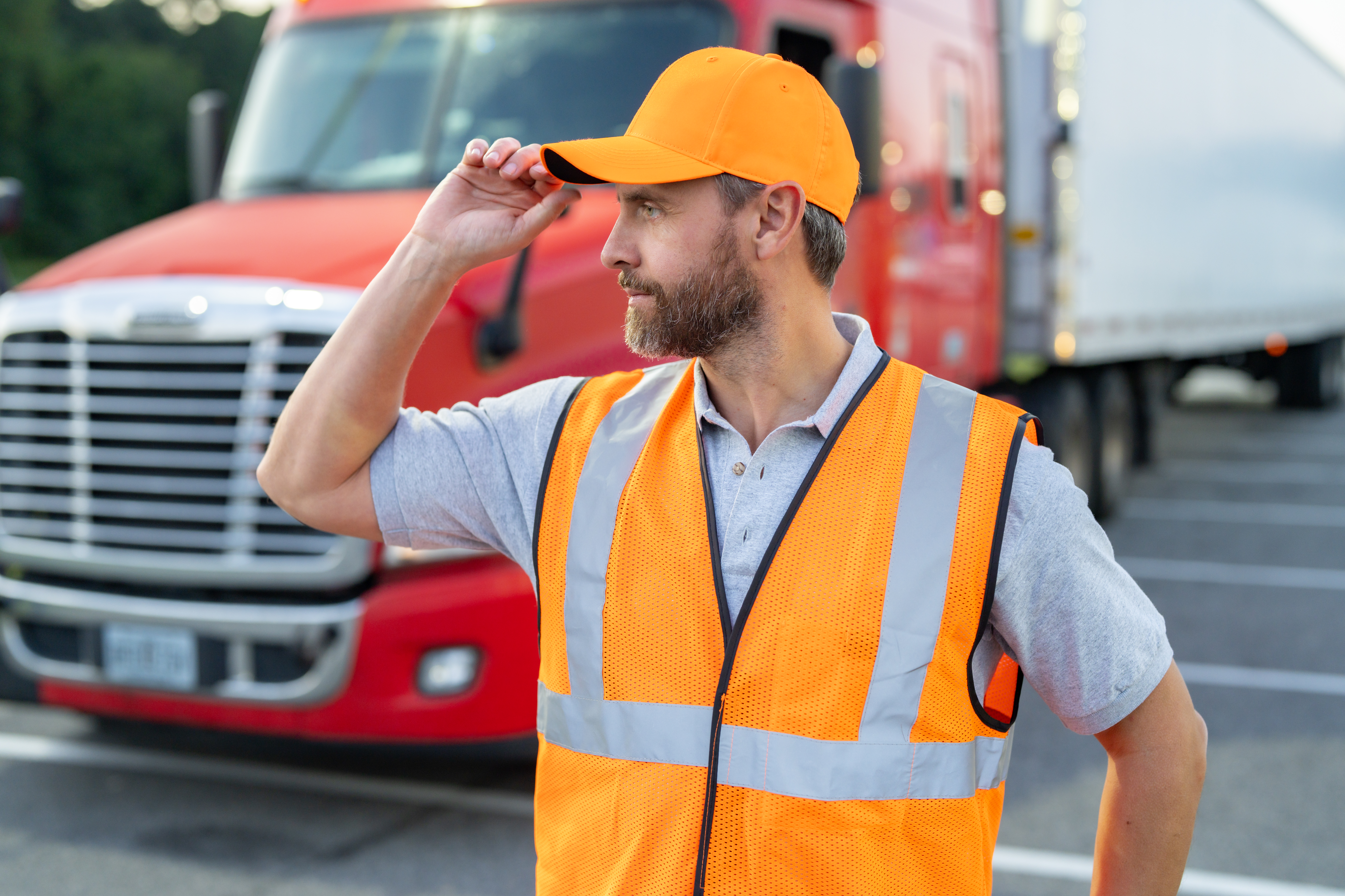 Truck driver wears a high visibility vest. Truck driver stands before a cargo truck. Professional truck driver works in transportation. Mature truckdriver represents logistics distribution